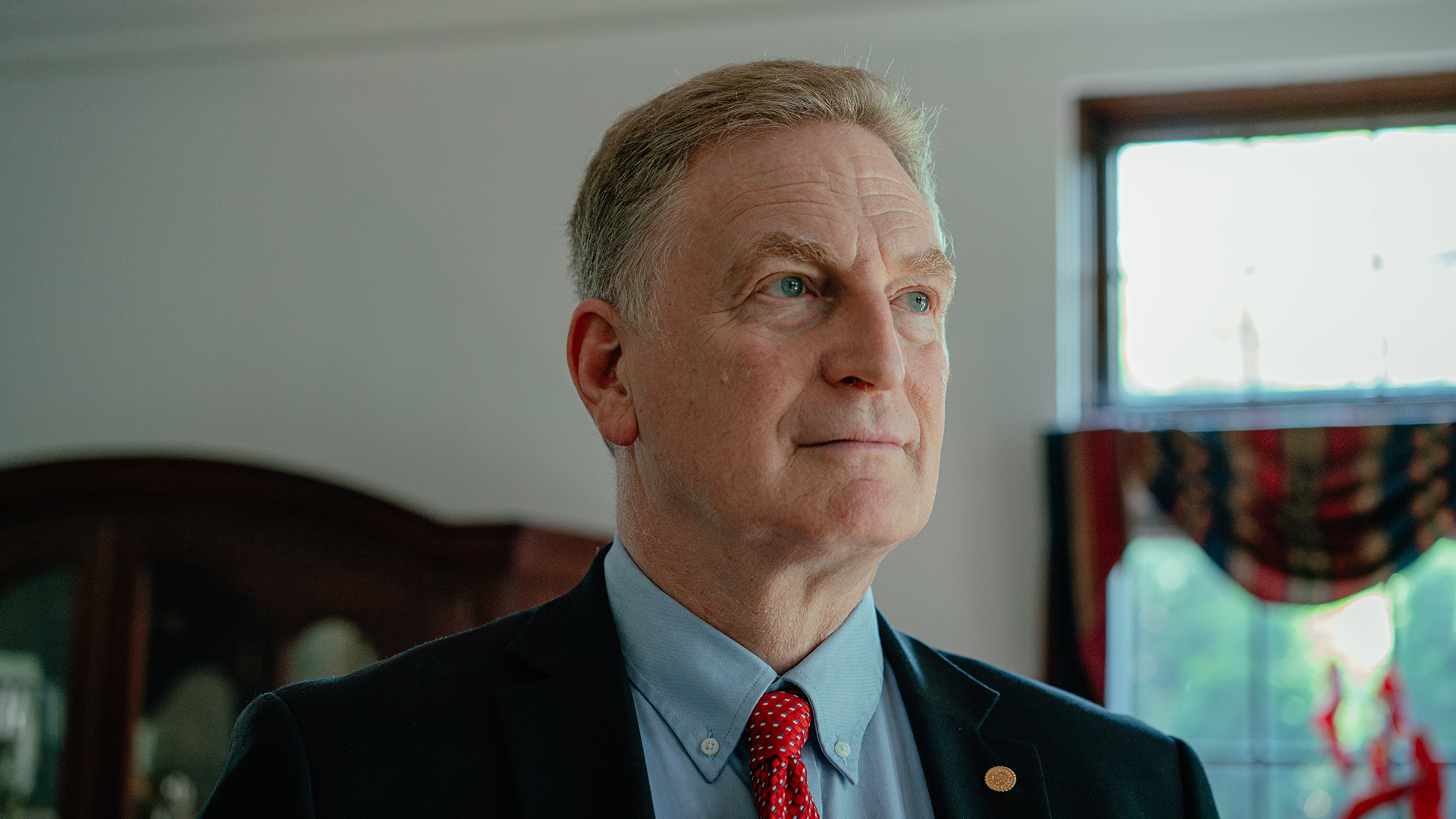 Sheldon Wasserman poses for a portrait while standing in a room with an out-of-focus wood cabinet and window in the background.