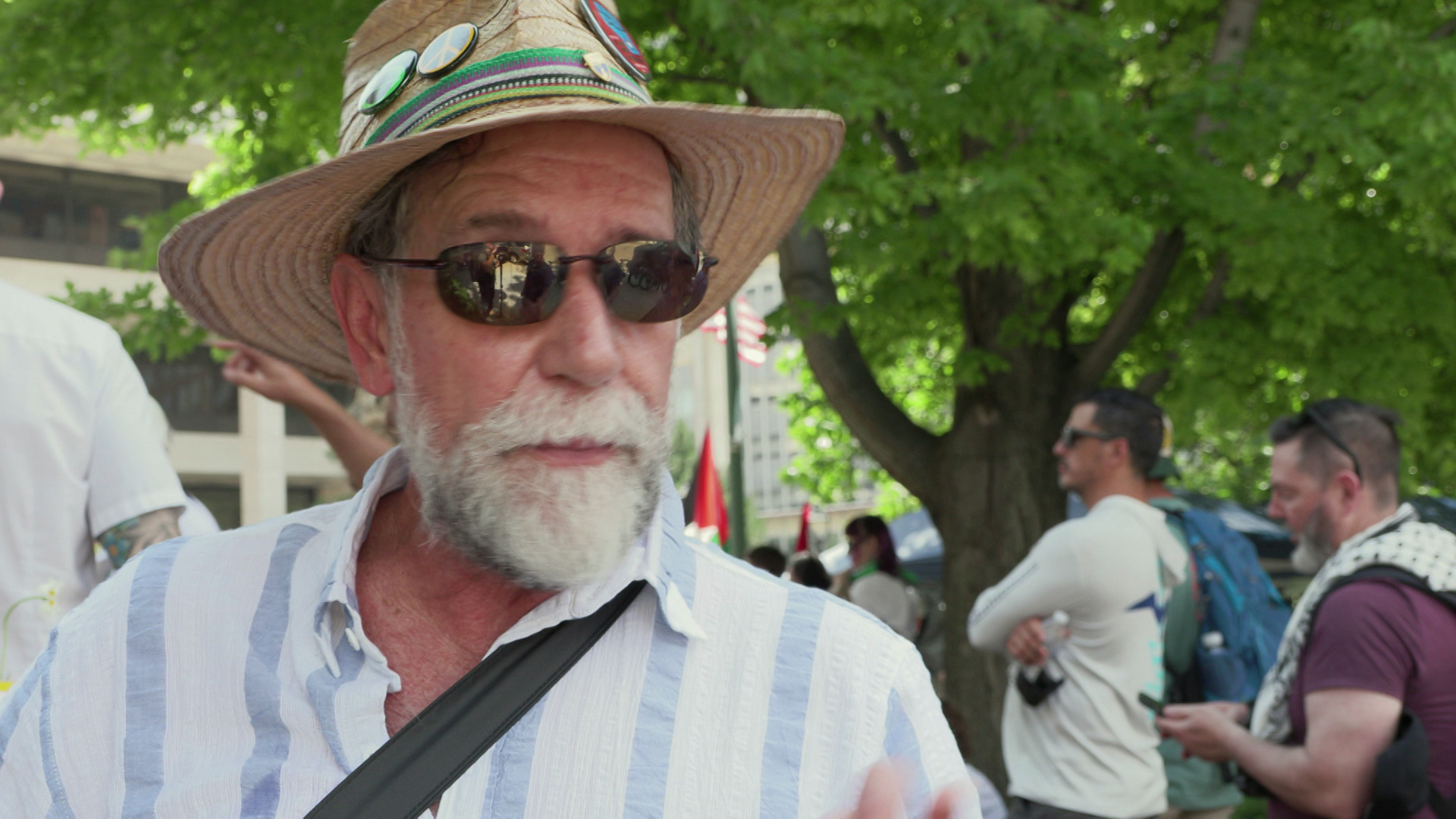 Ray Dall'Osto speaks outside while standing outside under trees with other people standing in the background.