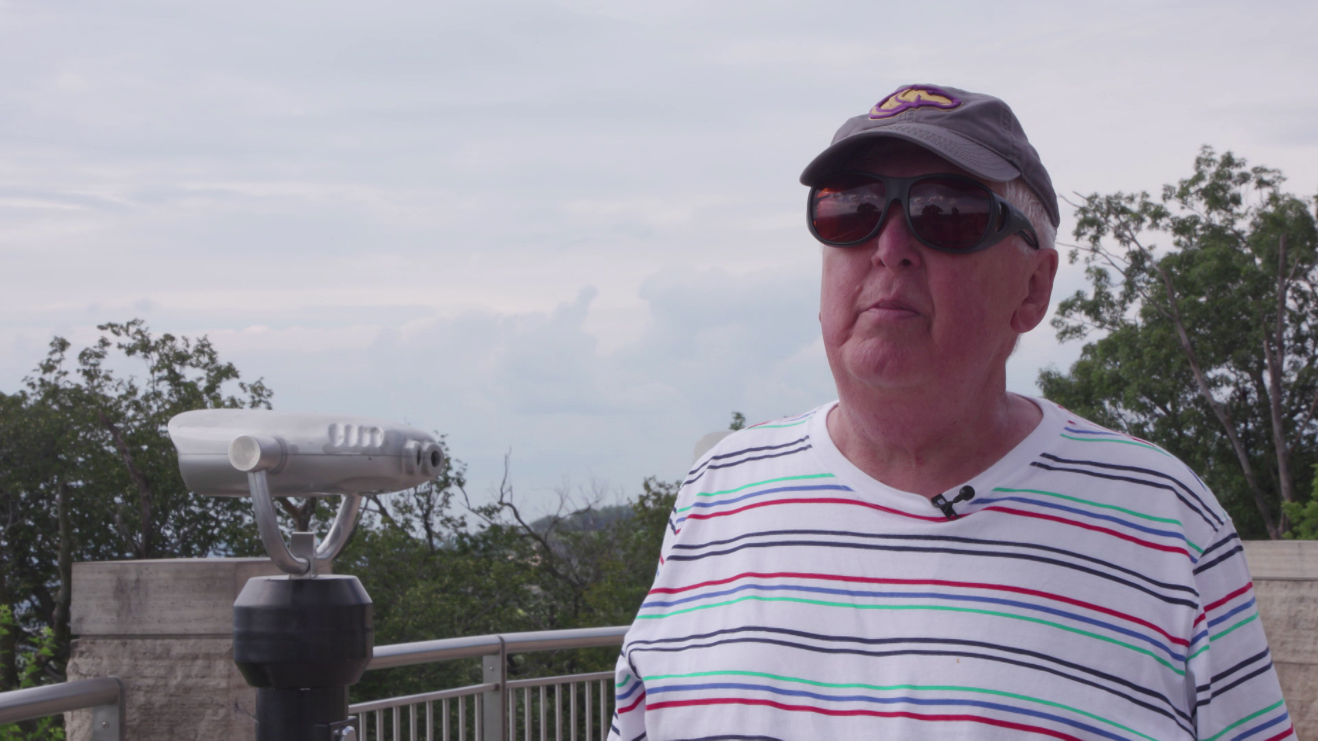 Michael Eve speaks while standing outside with trees and a tower viewer in the background.