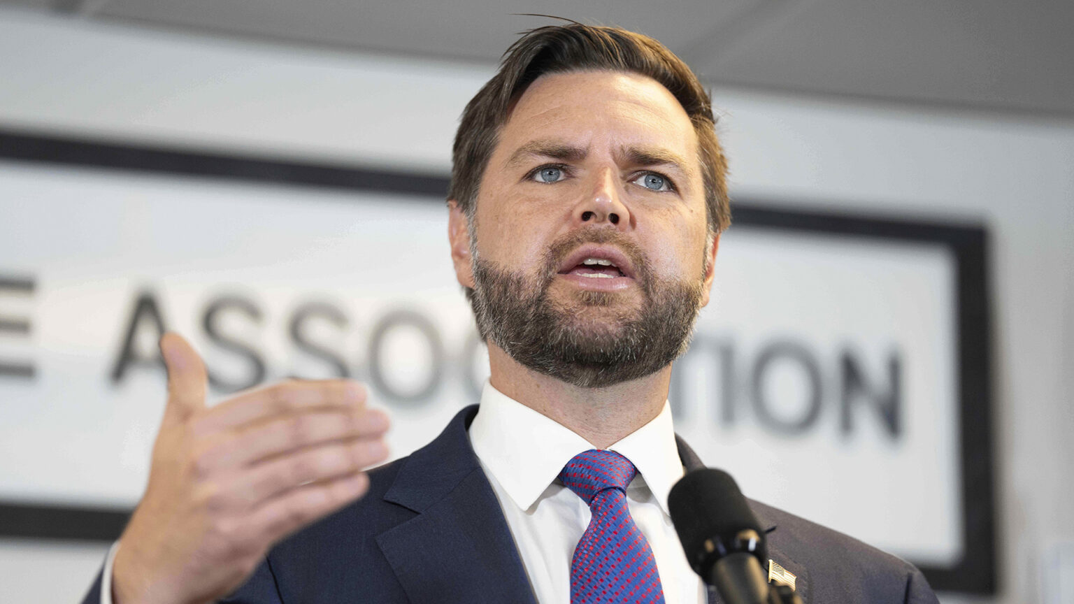 JD Vance gestures with his right hand while speaking into a microphone in a room.