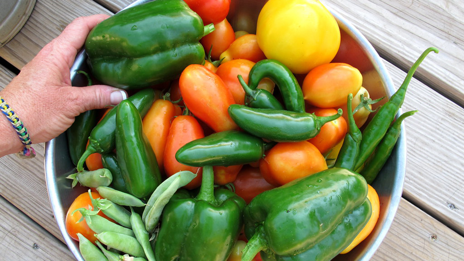 A hand reaches for a bowl filled with various vegetables.