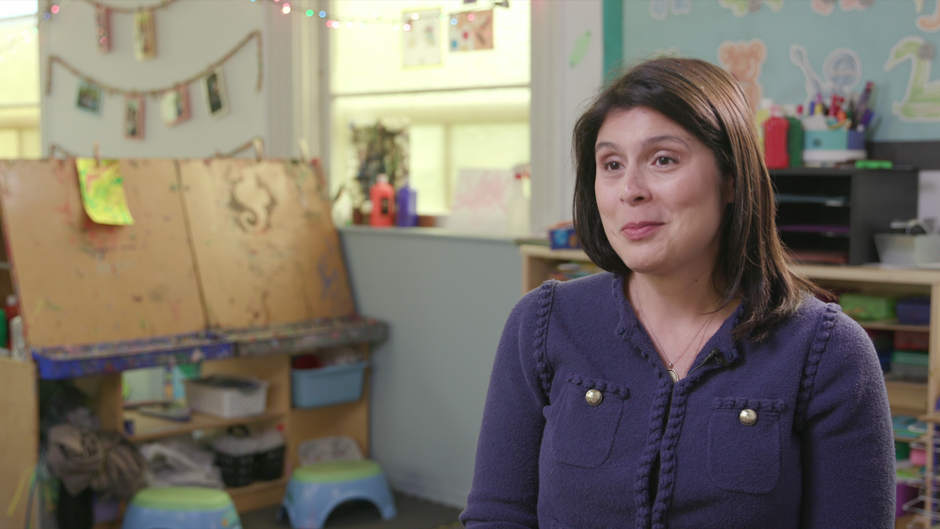 Amy Kloppenburg sits and speaks with arts supplies, easels, stools and artwork on the walls in the background.