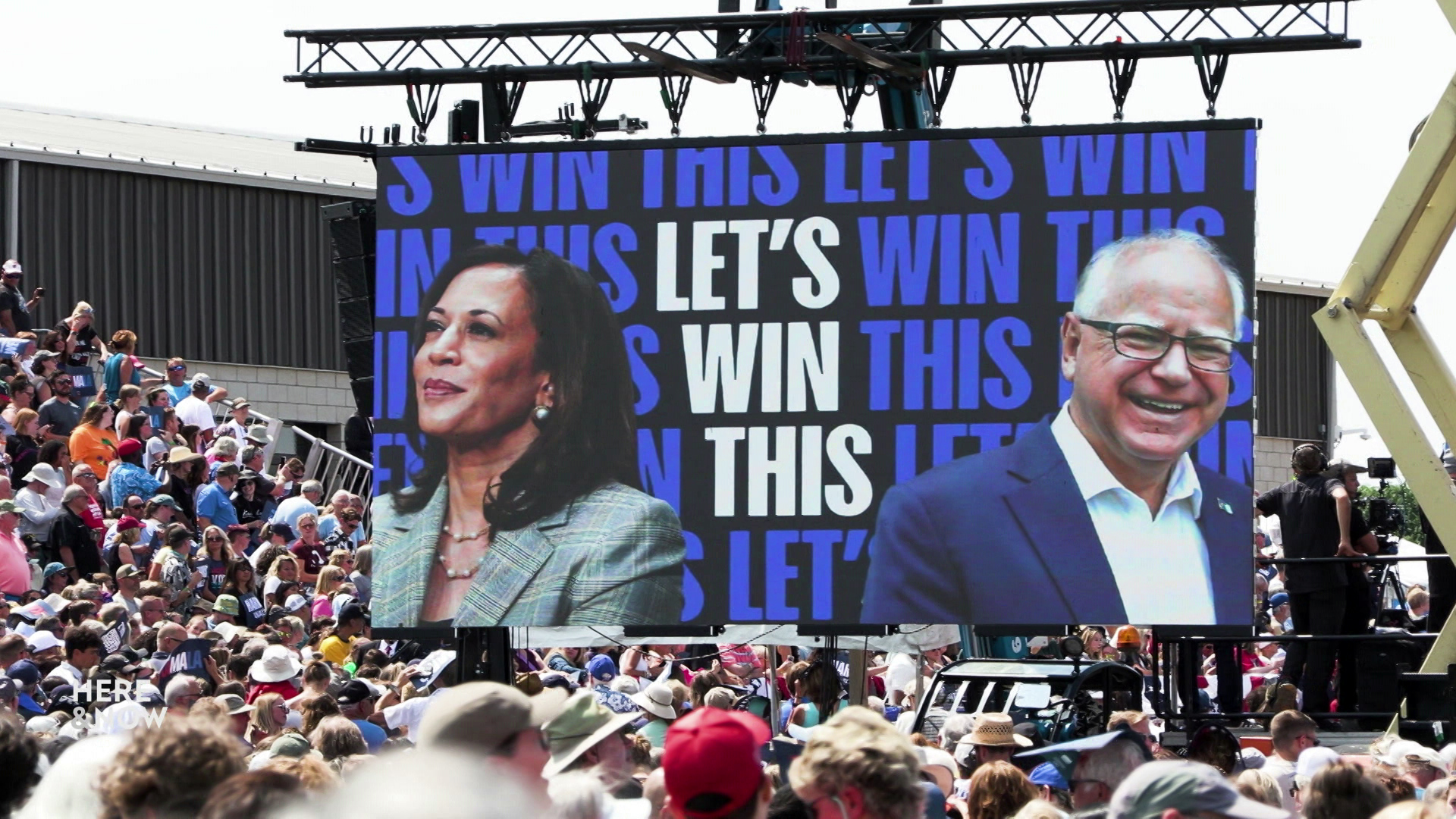 A large video screen depicts Kamala Harris and Tim Walz with graphics reading "Let's Win This" in the middle of a crowd of people seated and standing.