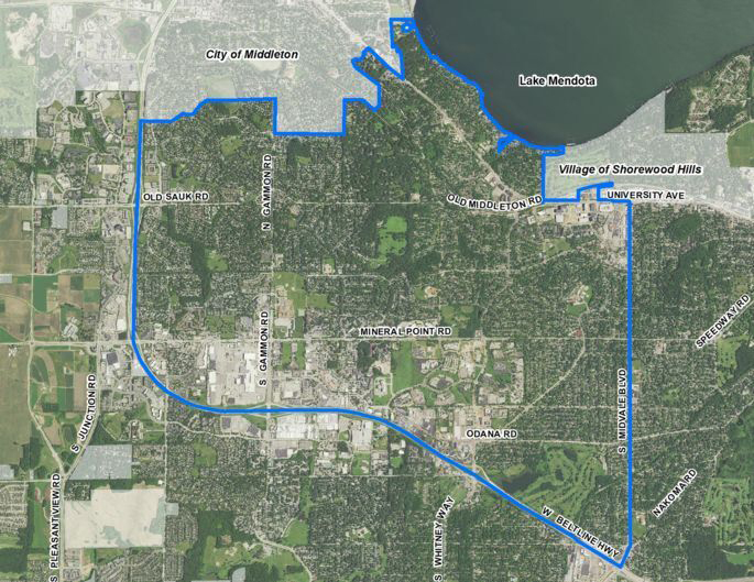 A satellite image of an urban area with different types of development, roads, parks, golf courses, farm fields and a body of water shows an outlined area, with labels marking different municipalities, street names and a lake.