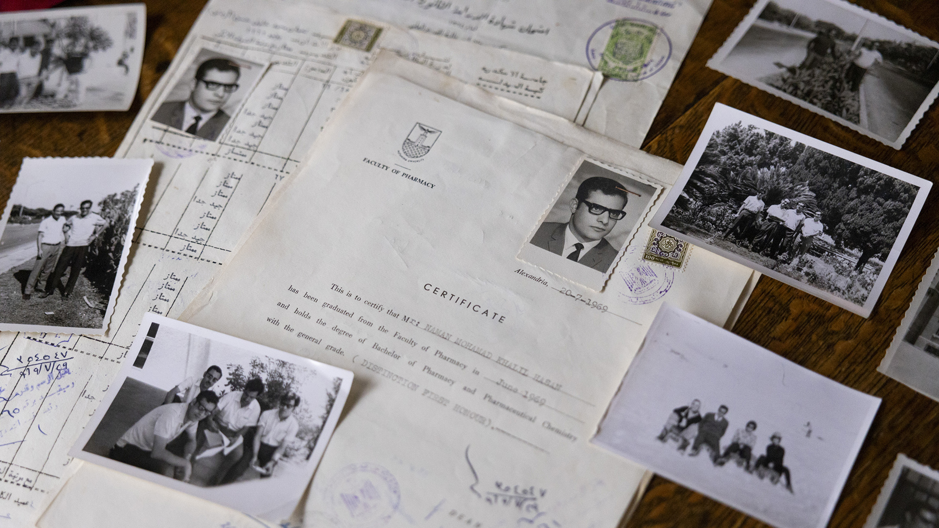 A variety of printed documents and black-and-white photos are arrayed on the surface of a wood table.