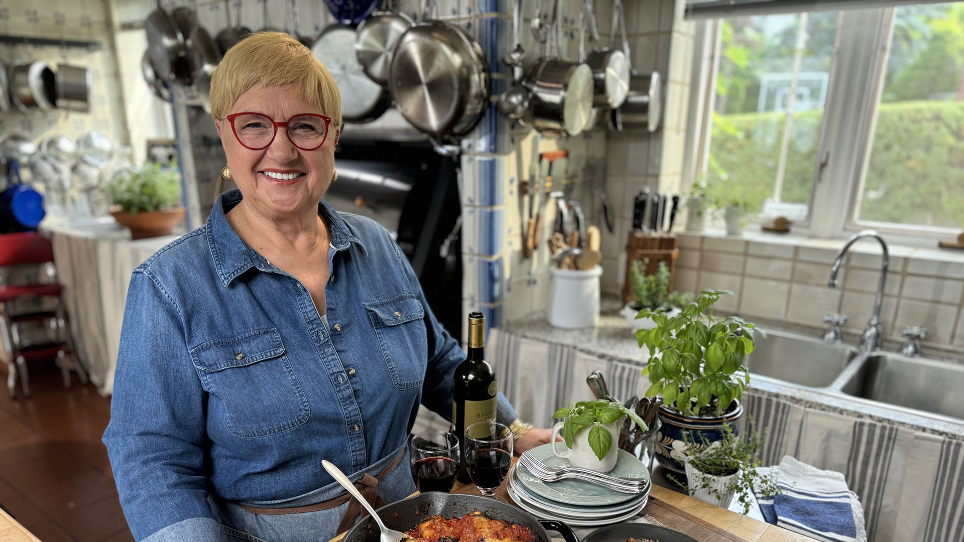 Chef Lidia Bastianich stands in front of a stovetop while cooking a meal.