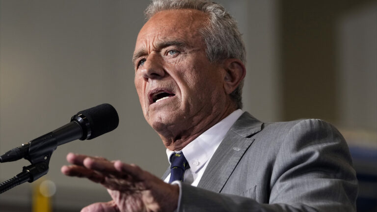 Robert F. Kennedy, Jr. gestures with his left hand while standing and speaking into a microphone.