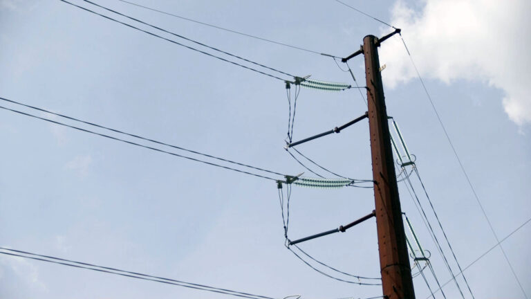 Multiple power lines attach to different tiers of a metal pole standing under a partly cloudy sky.