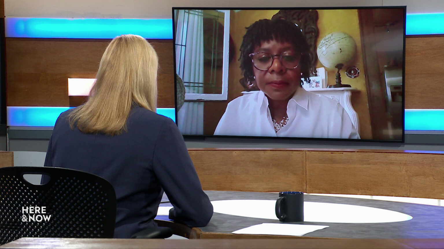 Frederica Freyberg sits at a desk on the Here & Now set and faces a video monitor showing an image of LaTonya Johnson.