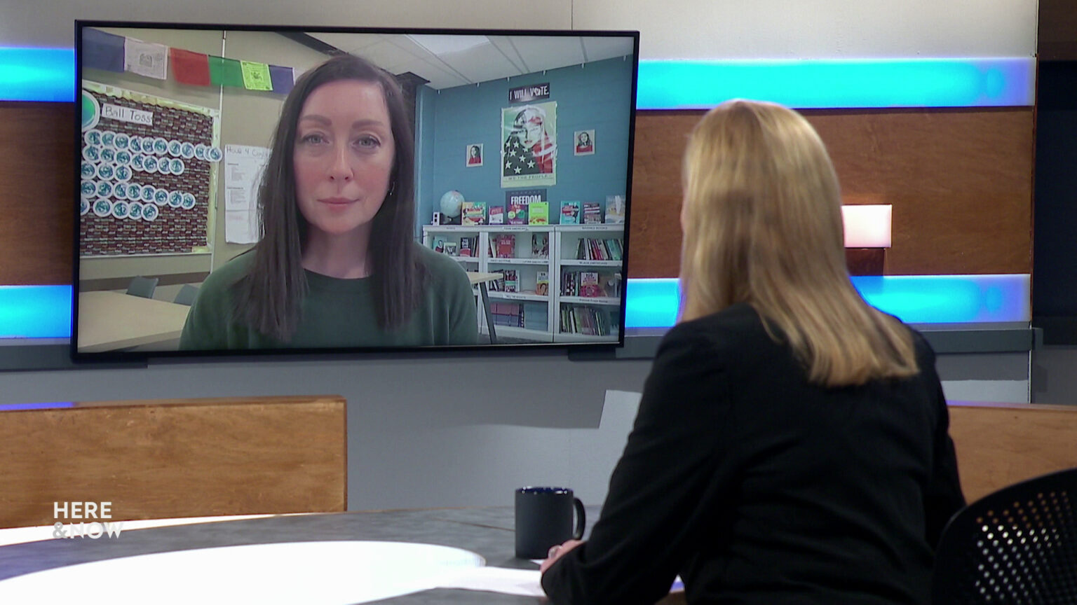 Frederica Freyberg sits at a desk on the Here & Now set and faces a video monitor showing an image of Sarah Kopplin.