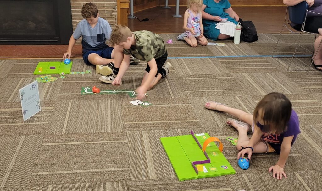 Children sit on the floor of a library, coding small plastic robot mice.