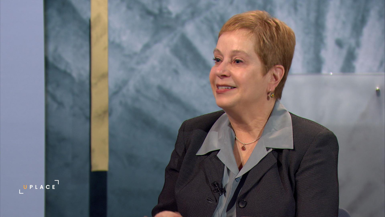 A woman smiles as she is being interviewed in a studio.