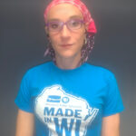 Person wearing a pink bandana, glasses, and a blue "Made in WI" Wisconsin Public Television t-shirt with a map outline of Wisconsin.