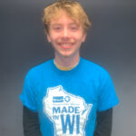 Smiling person wearing a blue "Made in WI" Wisconsin Public Television t-shirt with a map outline of Wisconsin.