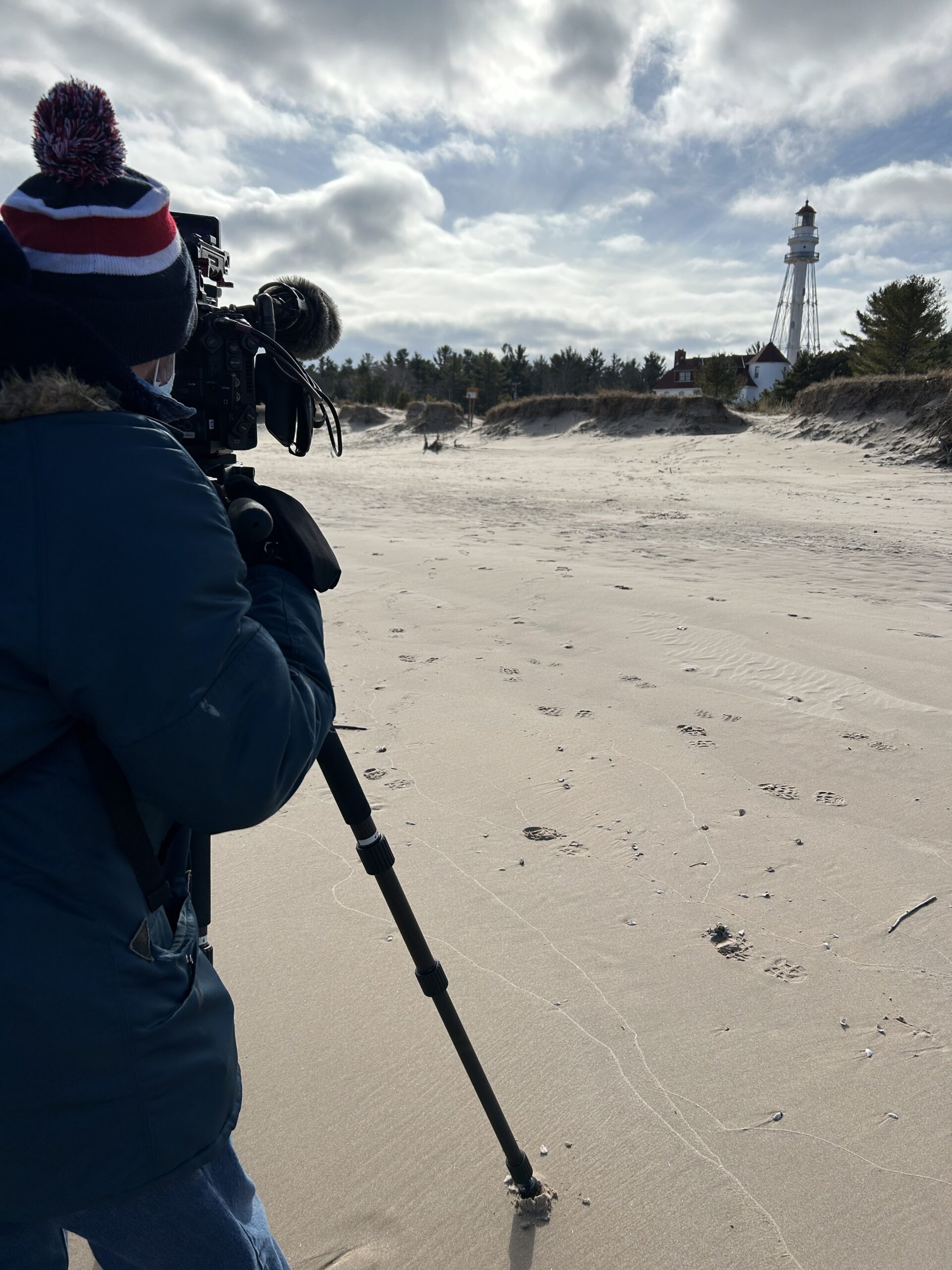 PBS Wisconsin producer Jeff Pfeiffer shooting footage for Wisconsin Lighthouses on the beach near a lighthouse.