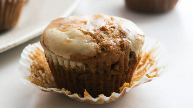 A glamor shot of a glazed pumpkin muffin with the paper liner pulled away slightly.