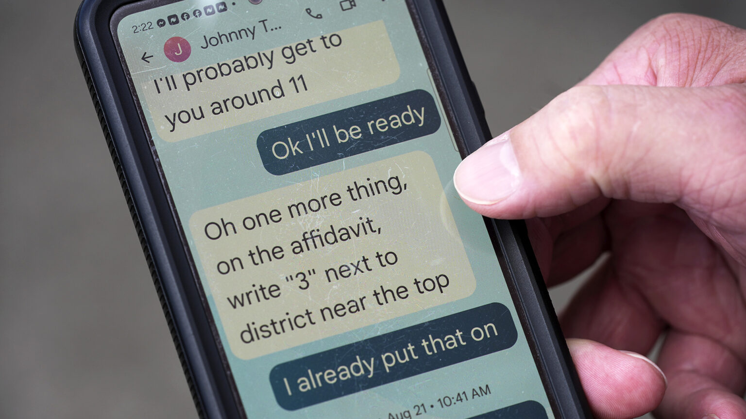 A hand holds a smartphone with the screen showing a text conversation.