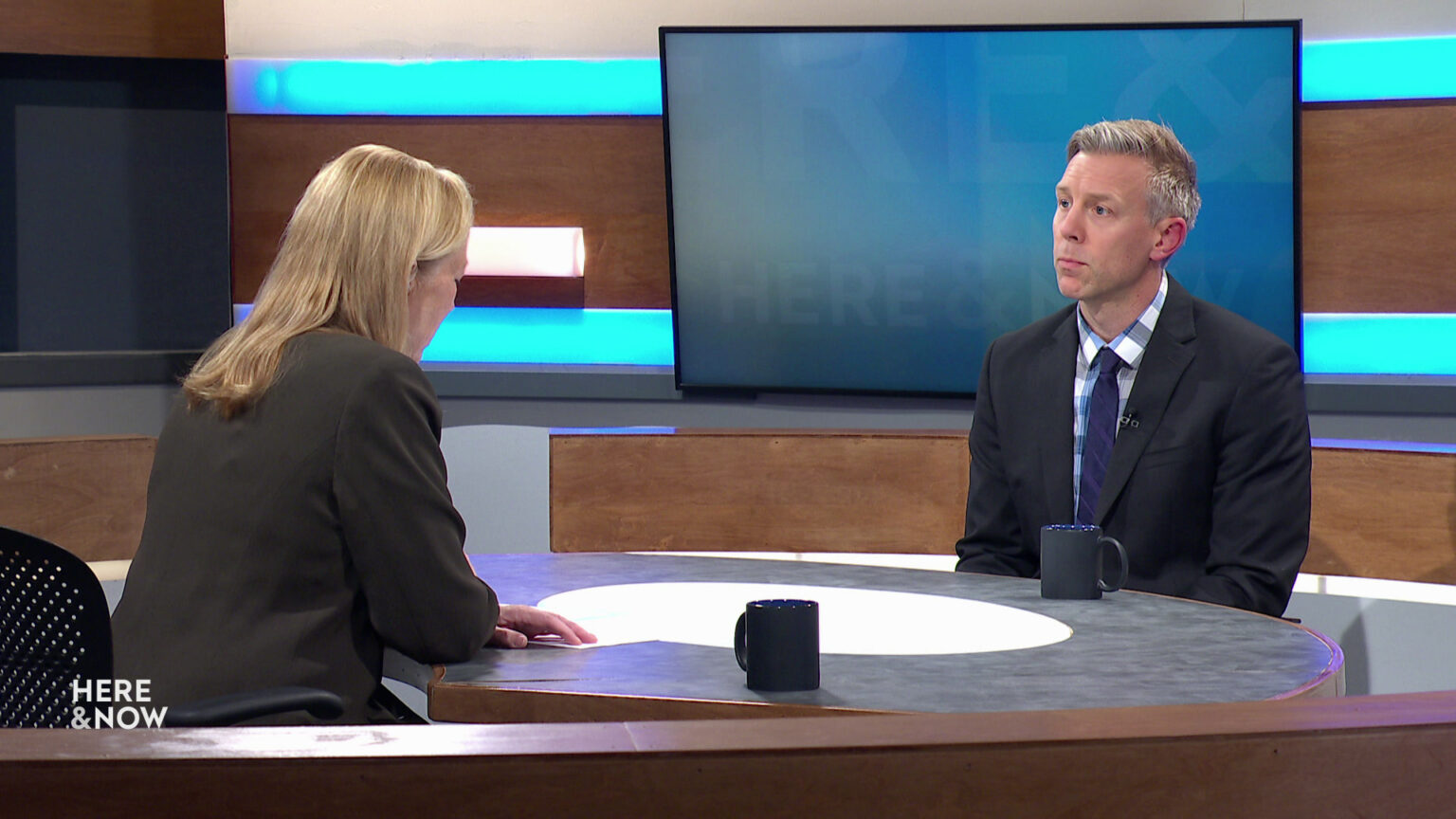 Frederica Freyberg and Nathan Kalmoe sit facing each other on the Here & Now set.