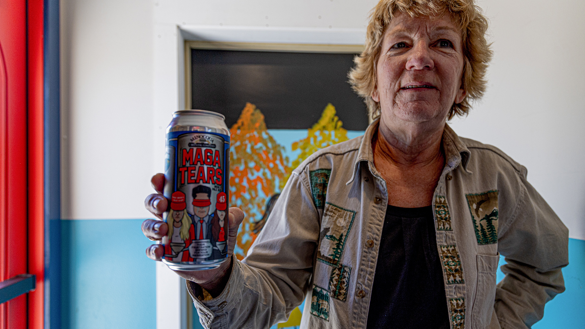 Sue Brisk stands and holds a 16-ounce beer can with a label reading "Maga Tears" in her right hand.