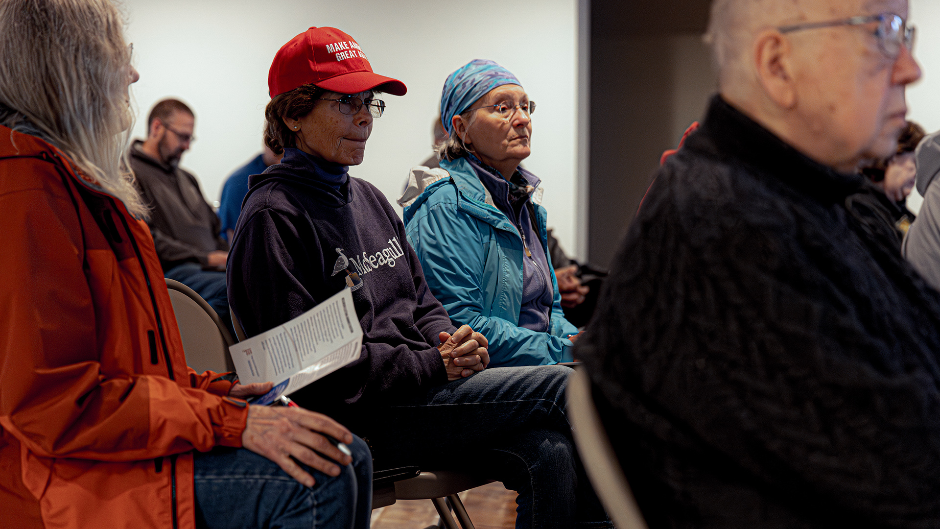 Terry Capsay sits in a folding chair with other people seated on either side and in front and behind of her.