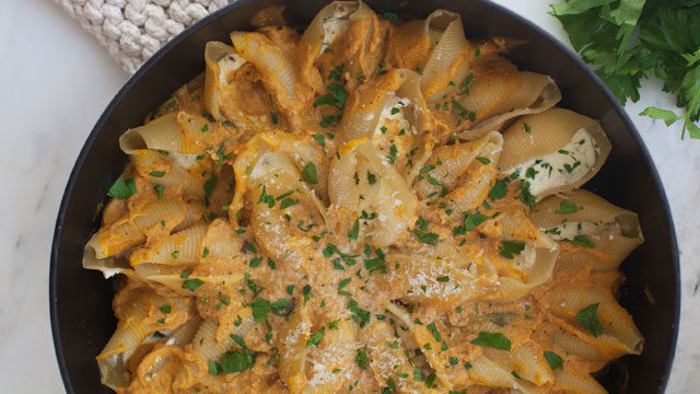 A glamor shot of a bowl of pasta shells with cheese melted on top, garnished with minced basil.