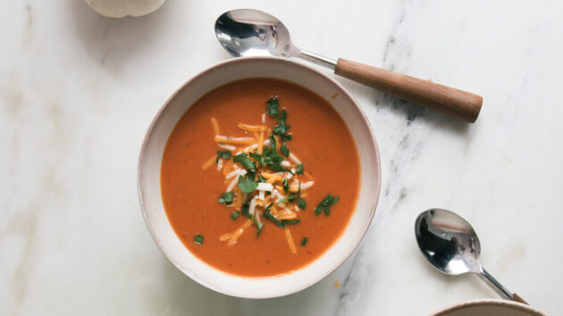 A glamor food shot of a bowl of pumpkin soup, garnished with cheese and parsley.