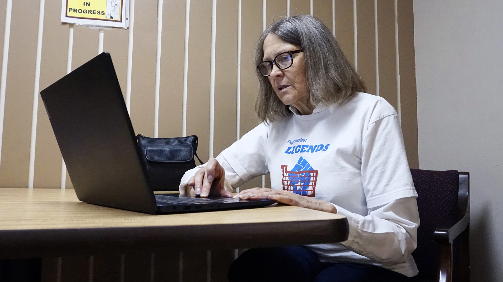 Linea Sundstrom uses a laptop computer while seated in a chair at a table next to a wall.