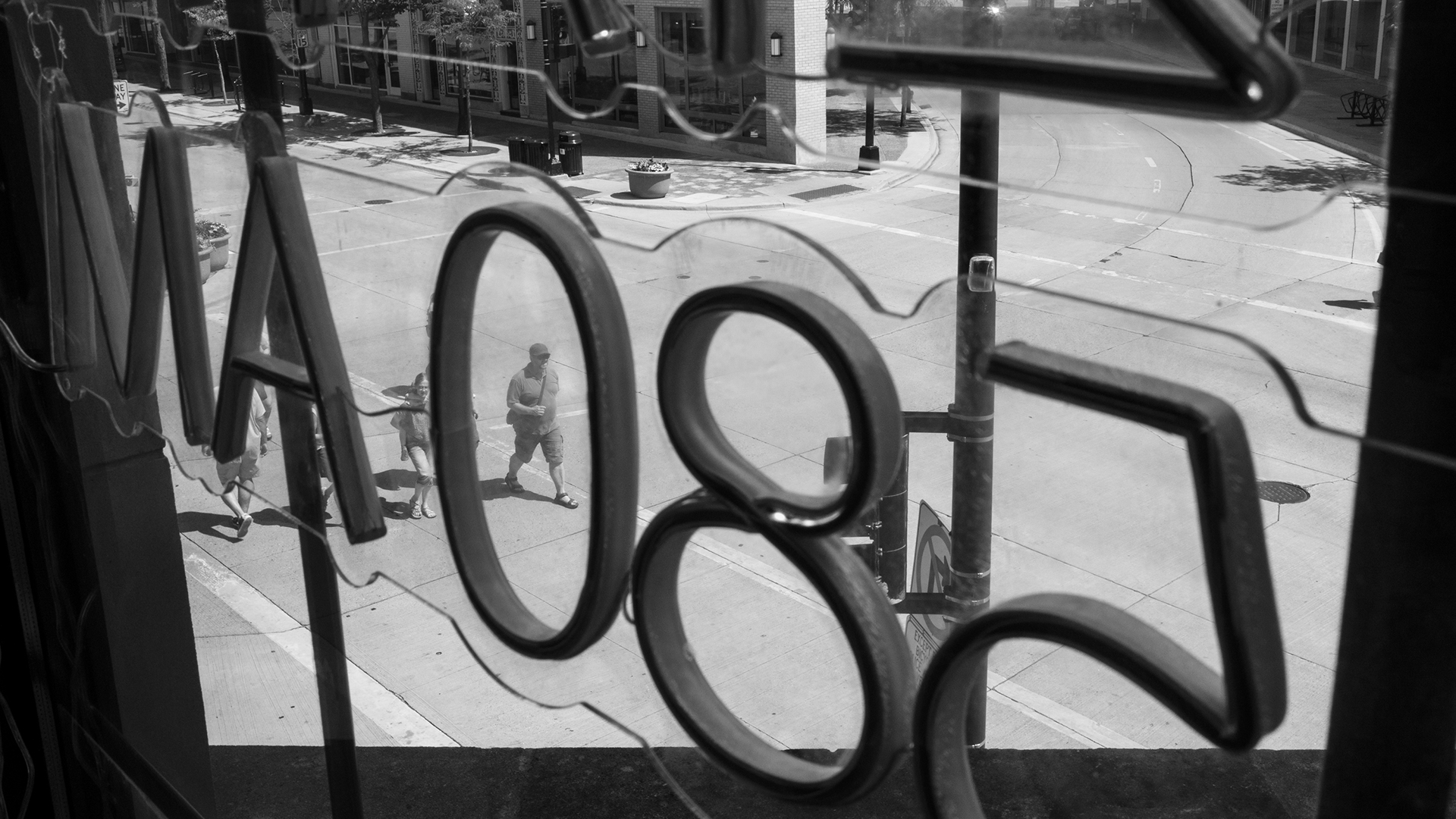 A sign with the broadcast call sign "580 AM" mounted on plastic is seen from behind and displayed in a window overlooking a street intersection, with walking pedestrians and buildings visible.