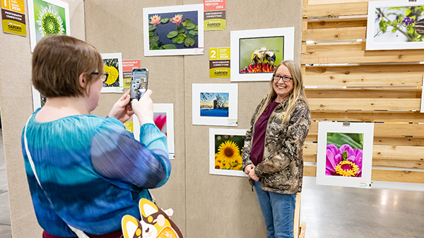 Julie Kissinger of Van Dyne, Wisconsin having her photo taken by a friend in front of her 2024 Expo photo entry - "It's a Sun-Dog Day" in the Phone and Tablet category.