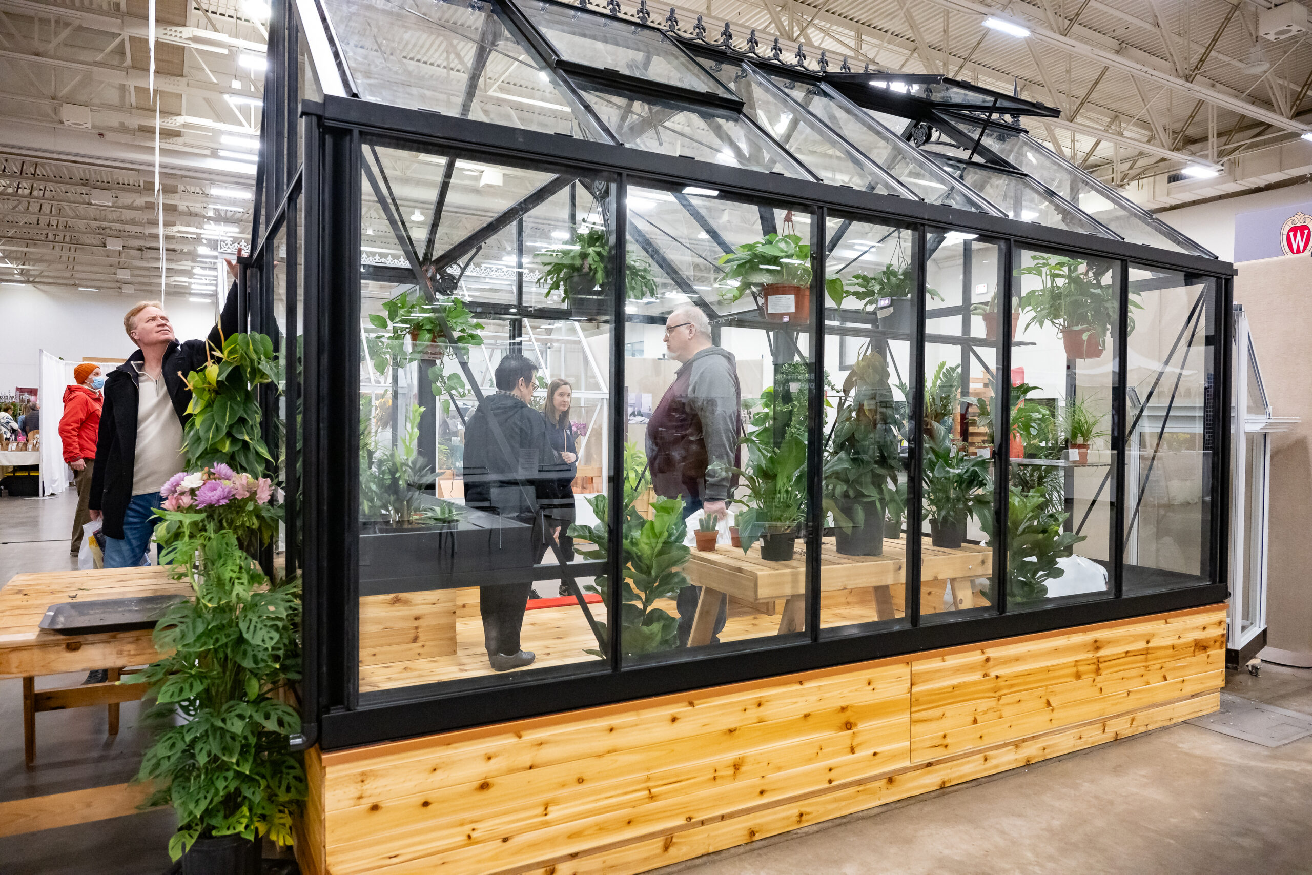 Three people tour a mobile greenhouse display at the 2024 Garden and Landscape Expo with a person inspecting the outside.