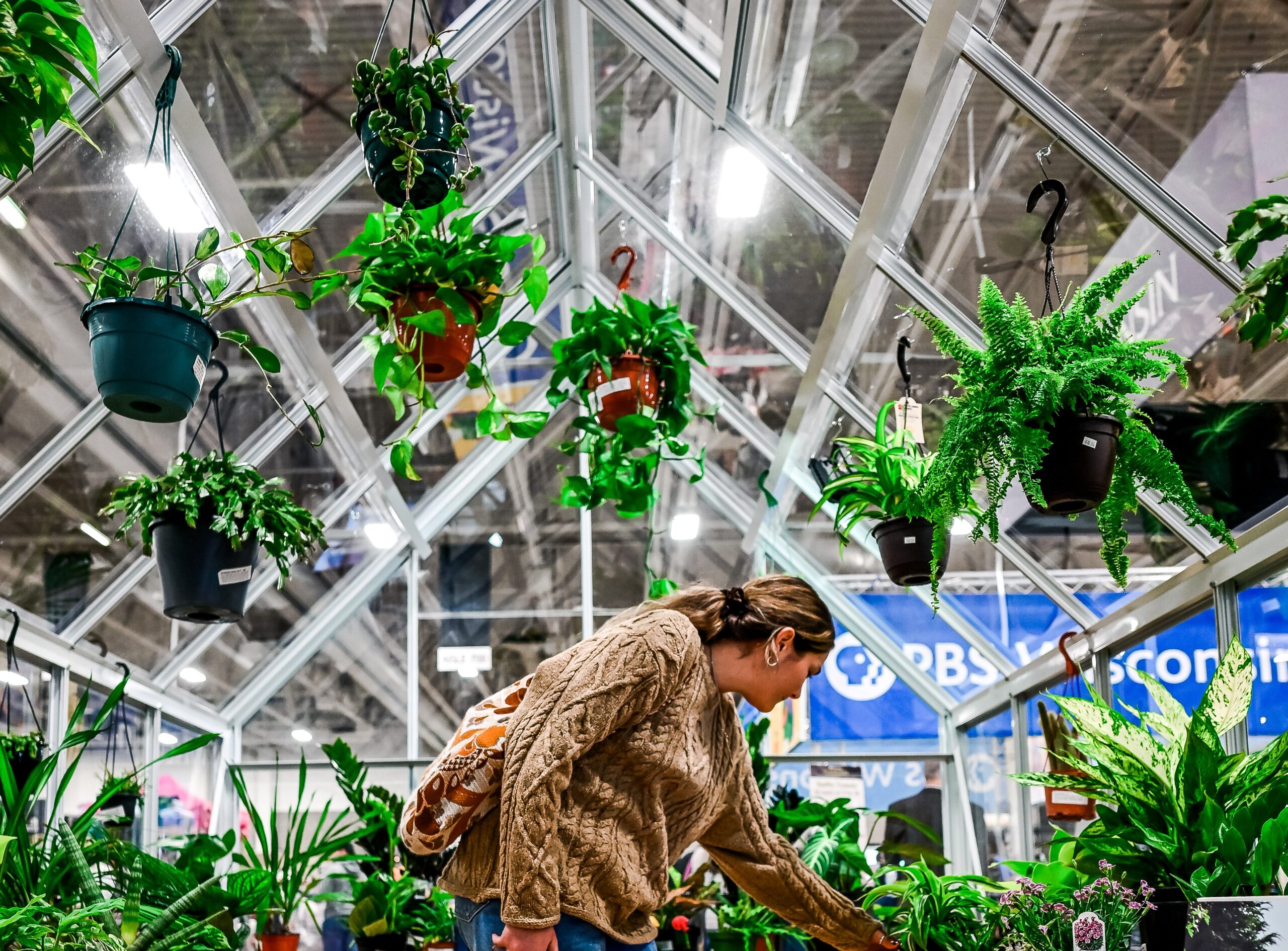 An image of a woman looking through plants in a greenhouse on the Garden Expo show floor.