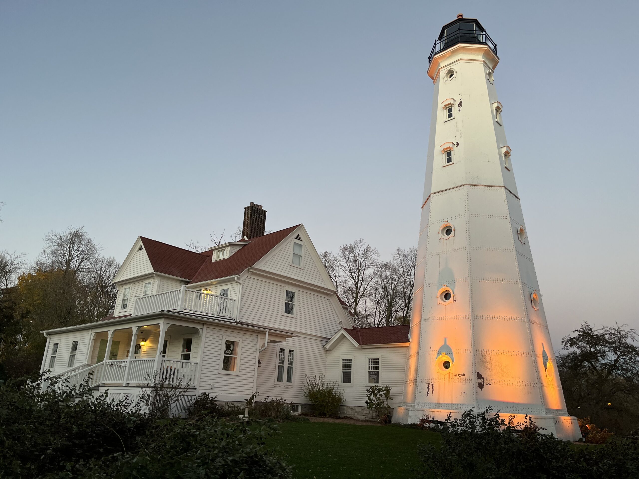 The North Point Lighthouse, a white two-story house with a burgundy roof next to a lighthouse with a tall white base capped by a burgundy top.