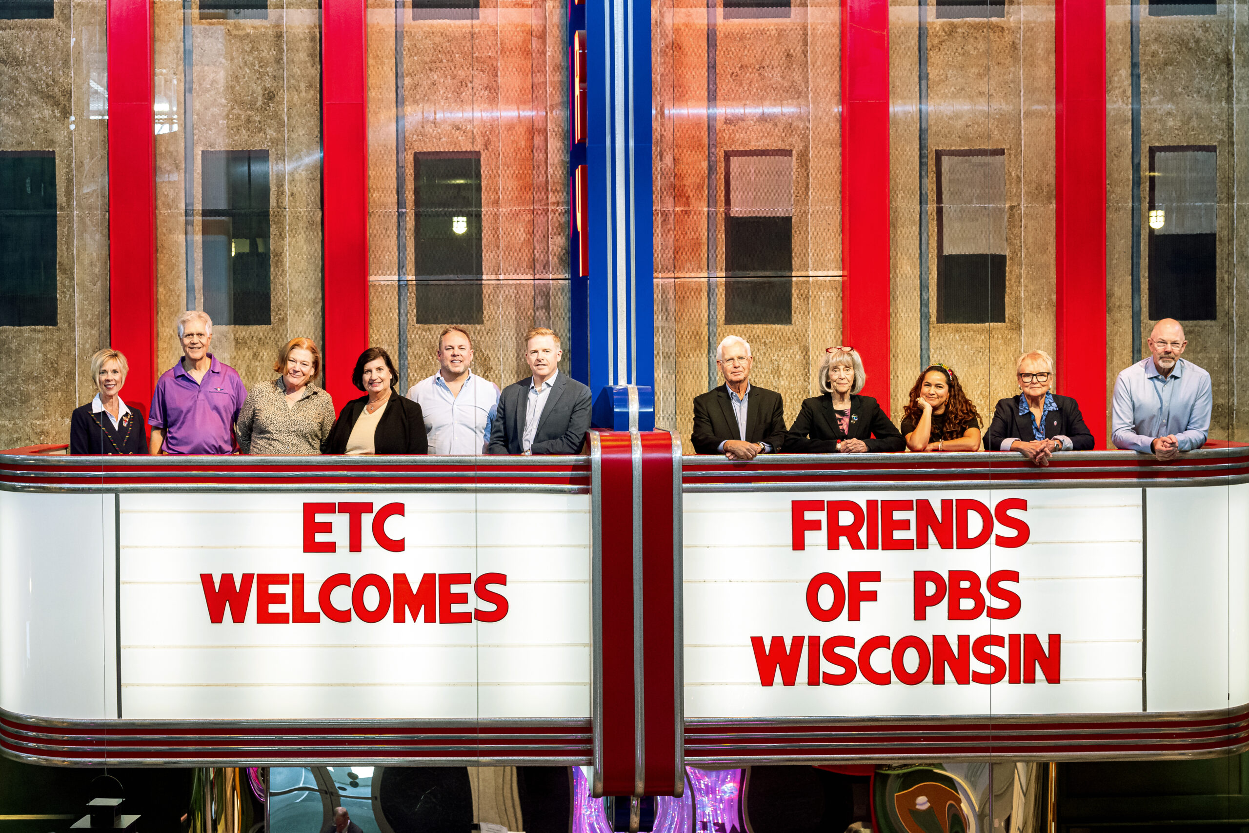 A marquee reads "ETC Welcomes Friends of PBS Wisconsin" while members of the Friends of PBS Wisconsin board post for a photo above the sign.