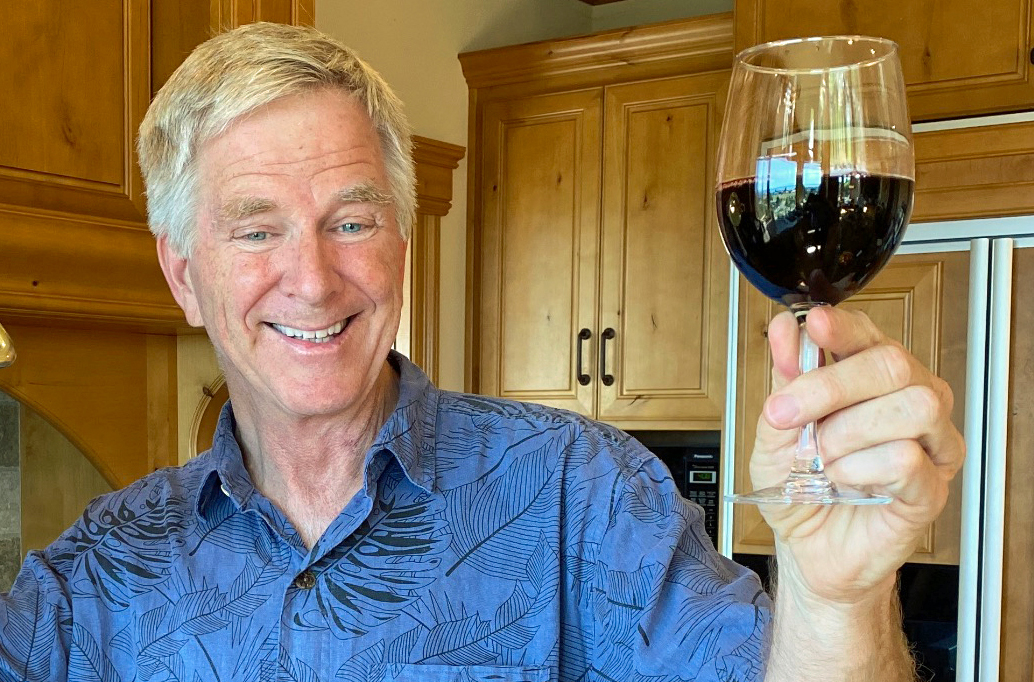 A man holds up a half a glass of red wine, in a toasting gesture.