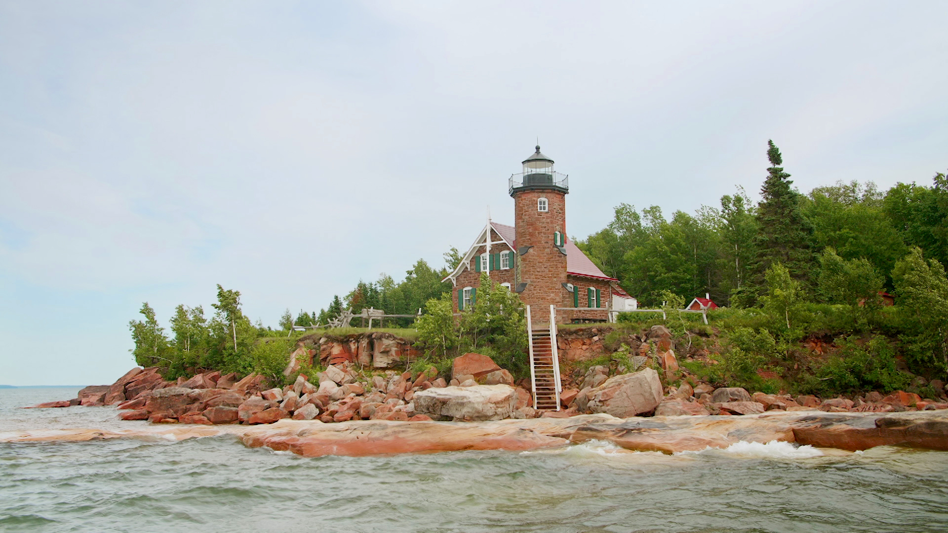 Shoreline in front of Sand Island Lighthouse with waves hitting against brown sandstone rocks.