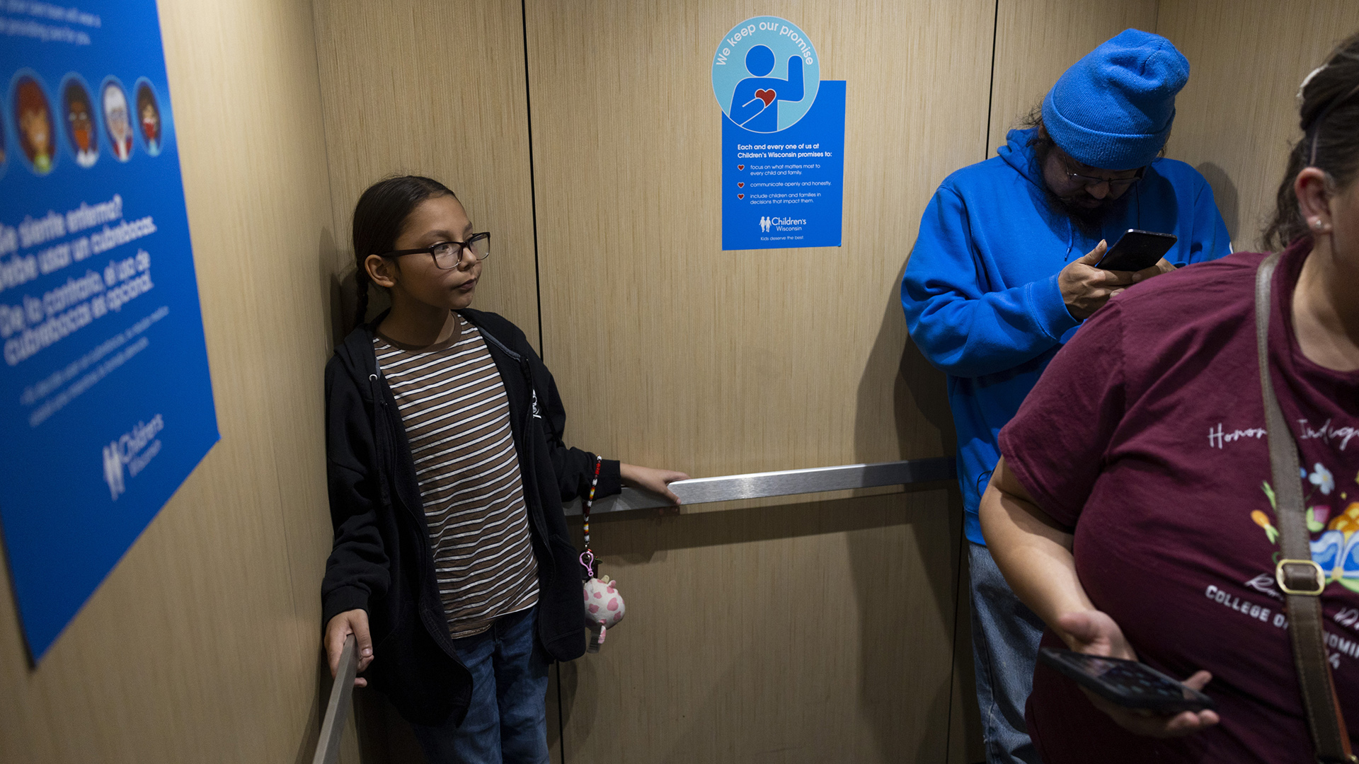 Nate, David and Lynda Hagen stand in an elevator with medical messages on decals on its wood veneer paneling.