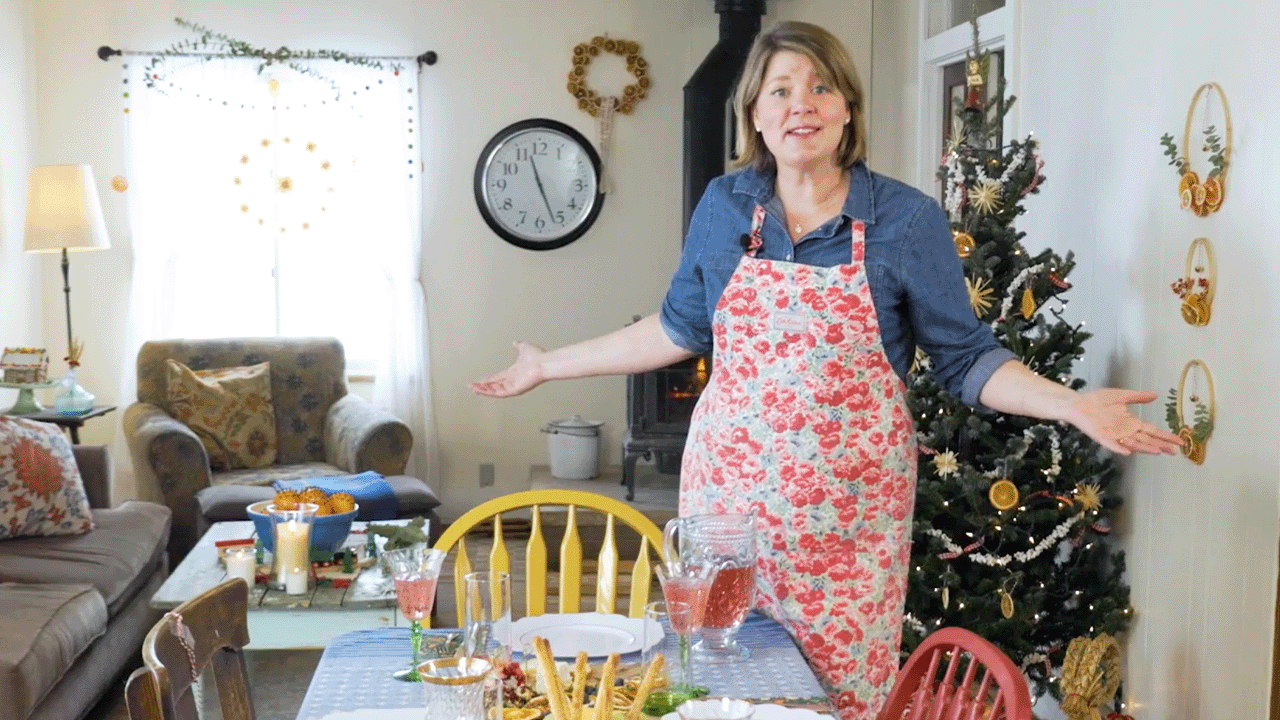 Inga stands in her dining room, preparing christmas foods at the table with a christmas tree in the background.