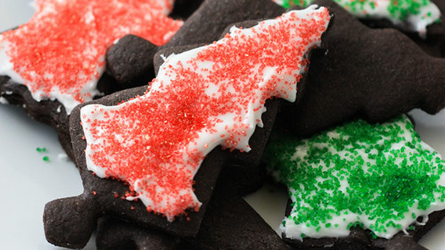 A glamor food shot of dark chocolate cinnamon holiday cookies, brownie-like cookies in the shape of Christmas trees with white icing and sprinkles.