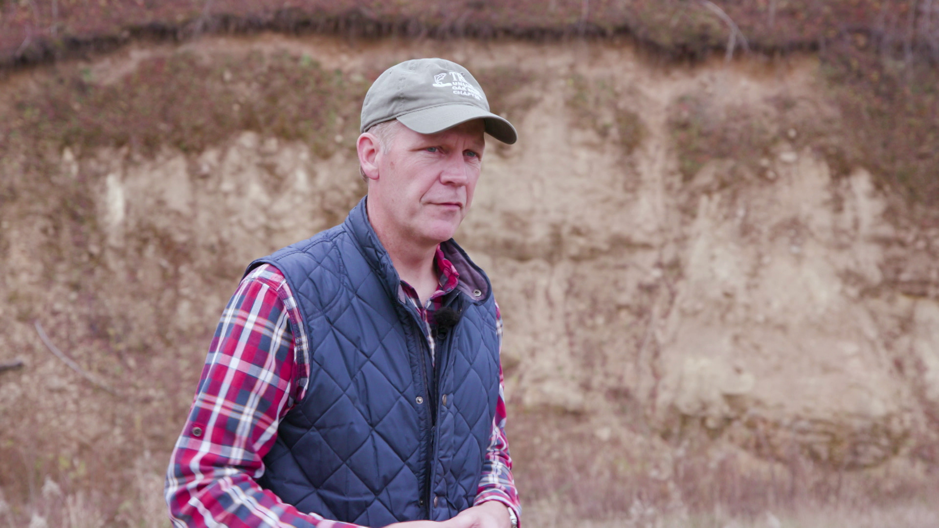 Bob Micheel speaks while standing outdoors with exposed earth in the background.