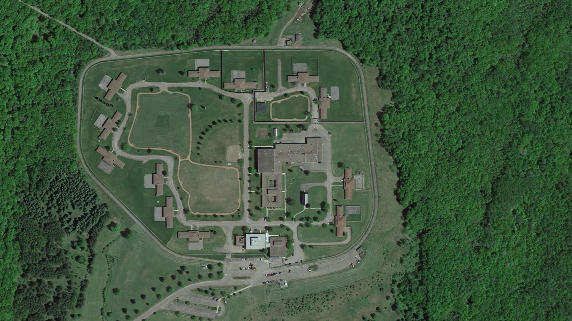 An aerial photo shows a group of buildings and connecting roads and parking lots surrounded by wooded areas.