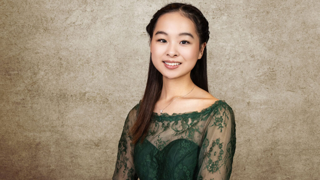 A young teenage girl in a formal dress smiles standing in a portrait studio.