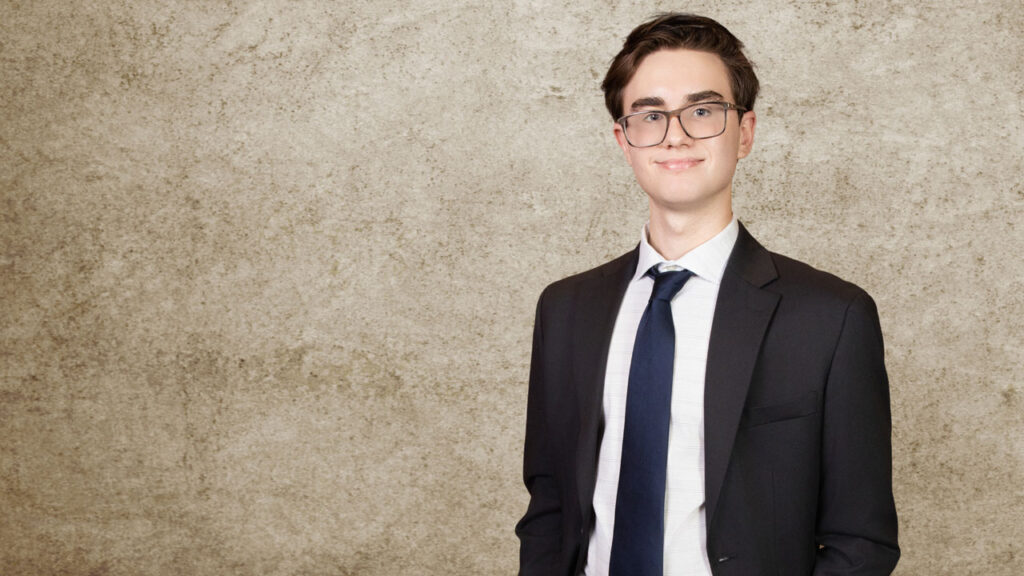 A teenage boy wearing a suit and tie smiles standing in a portrait studio.