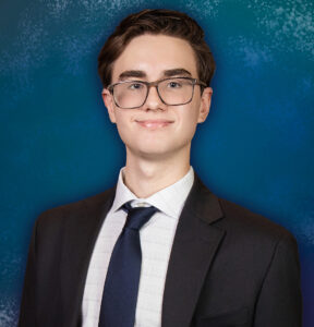 A teenage boy wearing a suit and tie smiles standing in a portrait studio.