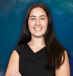 A young teenage girl in a formal dress smiles standing in a portrait studio.