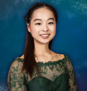 A young teenage girl in a formal dress smiles standing in a portrait studio.