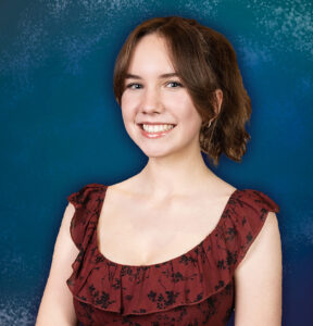 A young teenage girl in a formal dress smiles standing in a portrait studio.