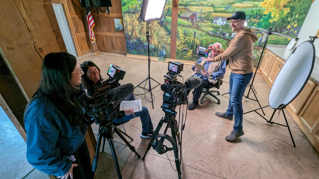 A camera crew prepares an interview in front of an indoor mural of a country scene.