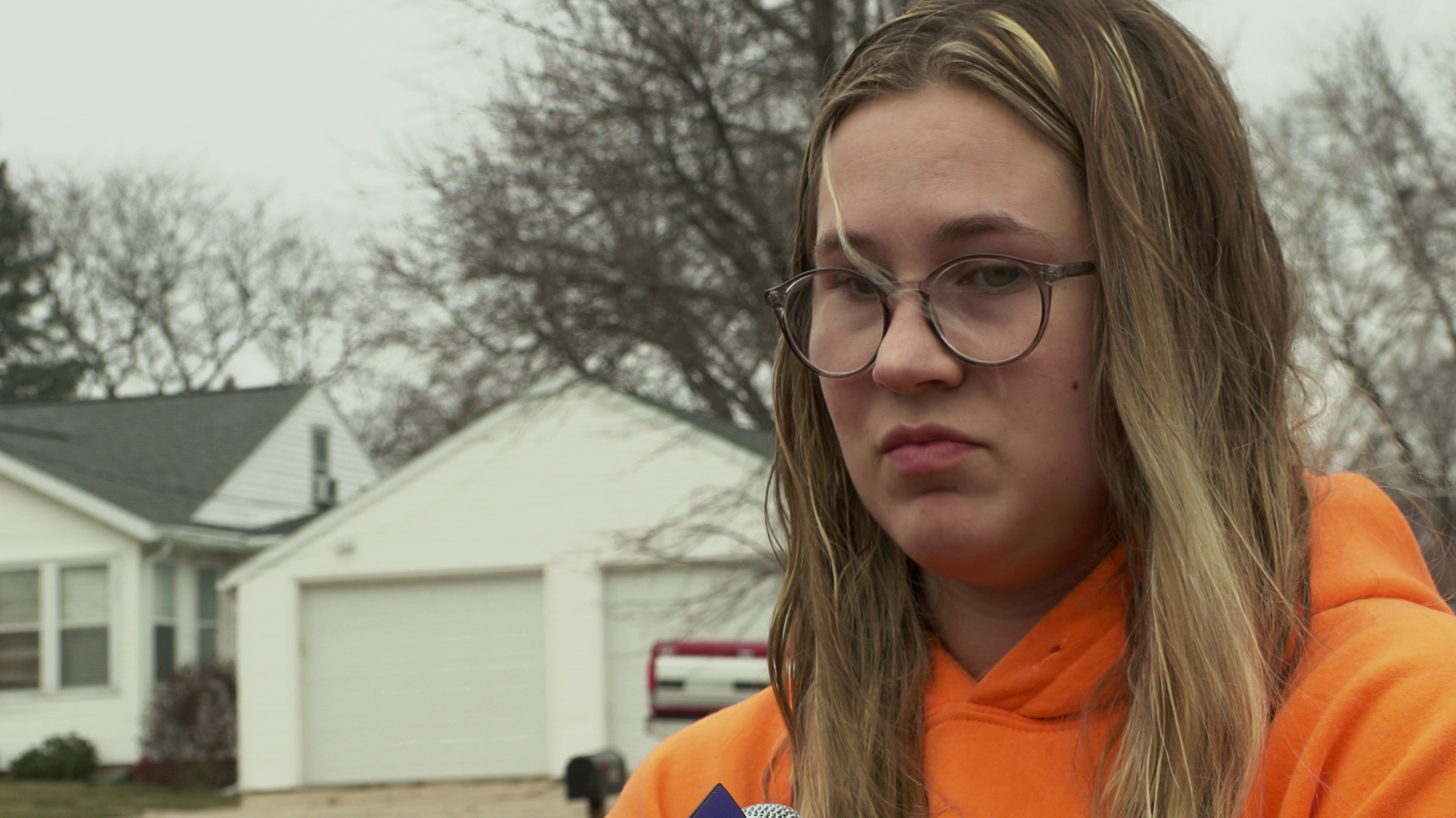 Mackenzie Truitt speaks while standing outdoors with trees, a house, garage and a parked vehicle in the background.