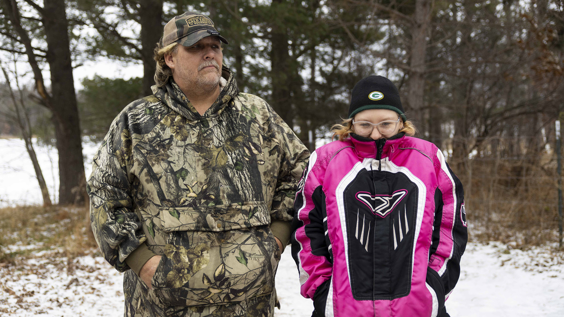 Eric Zieroth and Christina Hubbell stand outside wearing winter jackets, with snow-covered ground, trees and an ice-covered lake in the background.