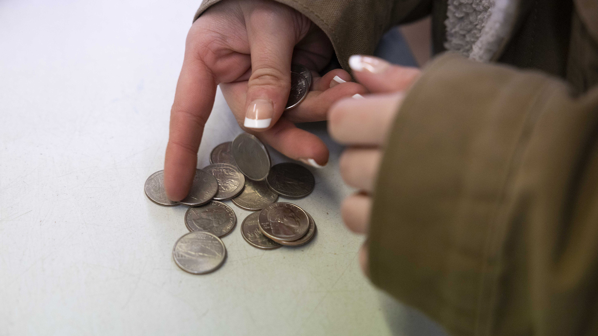 Christine Hubbell's hands count a small pile of quarters on a tabletop.